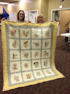 Cleo Lampos with her granddaughter and the finished quilt started by Cleo’s mother in the Dust Bowl with feed sack muslin squares and transfers from newspapers.