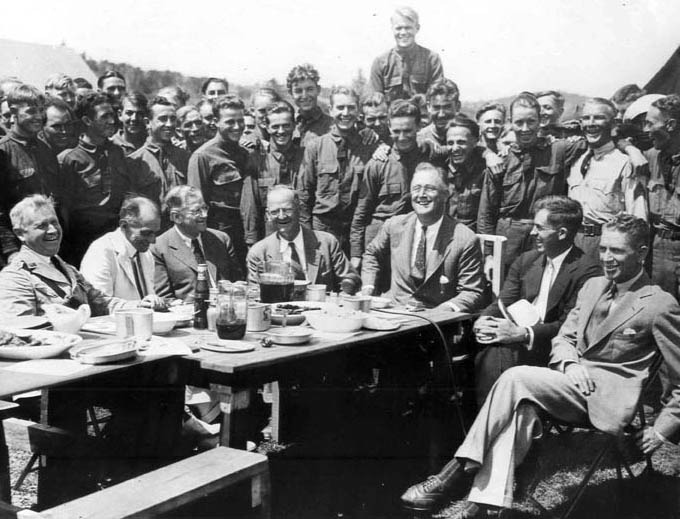 President Franklin Roosevelt visited with CCC enrollees near Camp Roosevelt on August 12, 1933, at Big Meadows, Skyland Drive, Virginia. Seated from left are Maj. Gen. Paul B. Malone, Louis M. Howe, Harold L. Ickes, Robert Fechner, FDR, Henry A. Wallace, and Rexford Tugwell. (35-GE-3A-5)